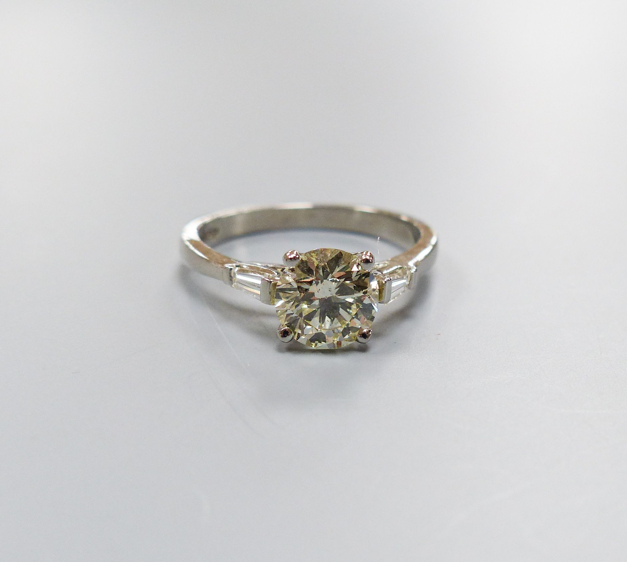 A modern platinum and single stone diamond ring, with trapeze cut diamond set shoulders, size O, gross weight 4.3 grams